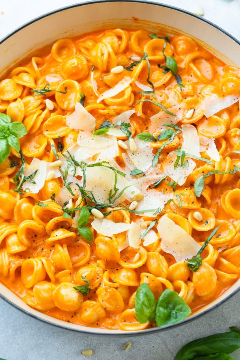 creamy red pepper pasta topped with large pieces of shaved parmesan cheese and fresh basil