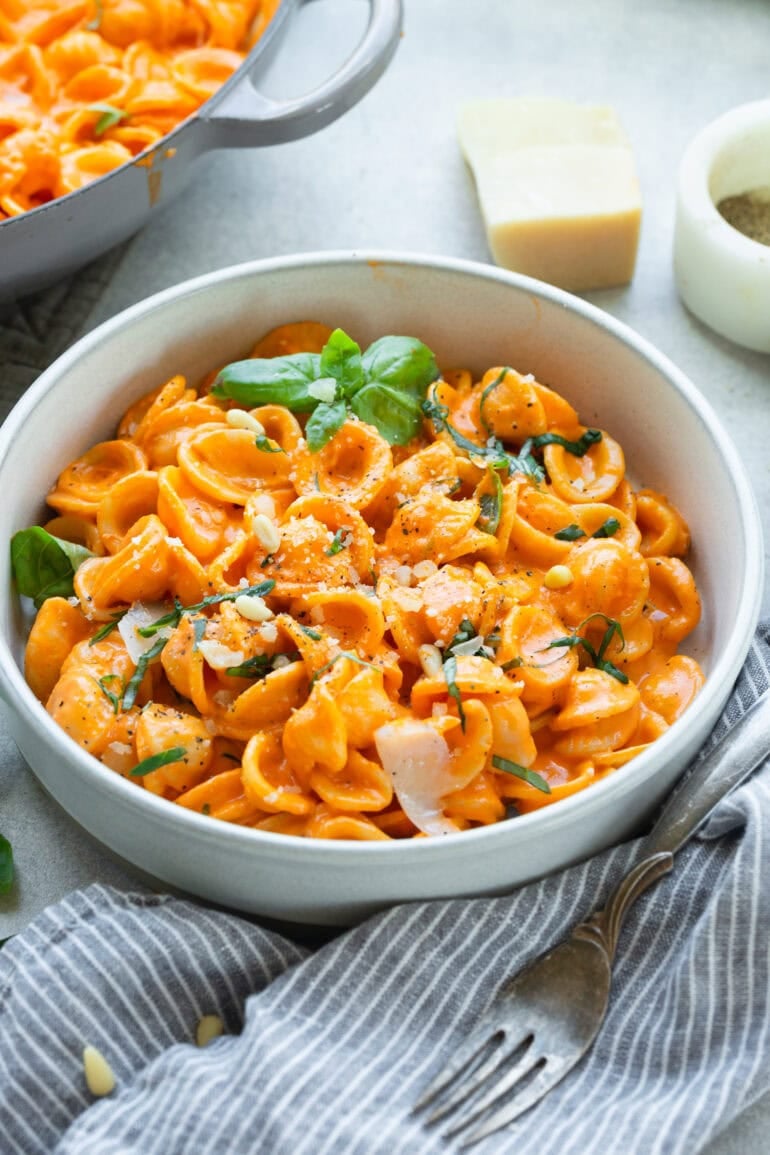 a bowl of creamy red pepper pasta topped with fresh basil and shaved parmesan cheese