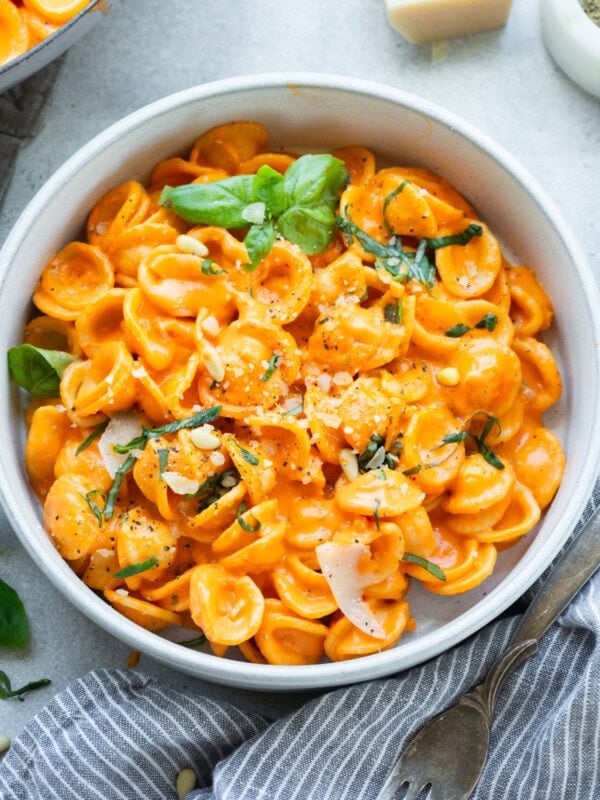 a large bowl of cooked orecchiette pasta tossed with roasted red pepper sauce and topped with chopped herbs