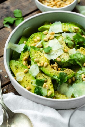 a bowl of avocado salad mixed with toasted pine nuts and chunks of manchego cheese topped with cilantro.