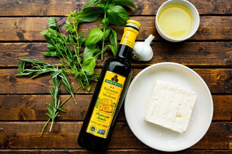 a crunchy crostini being dipped into a block of feta cheese covered with herby olive oil