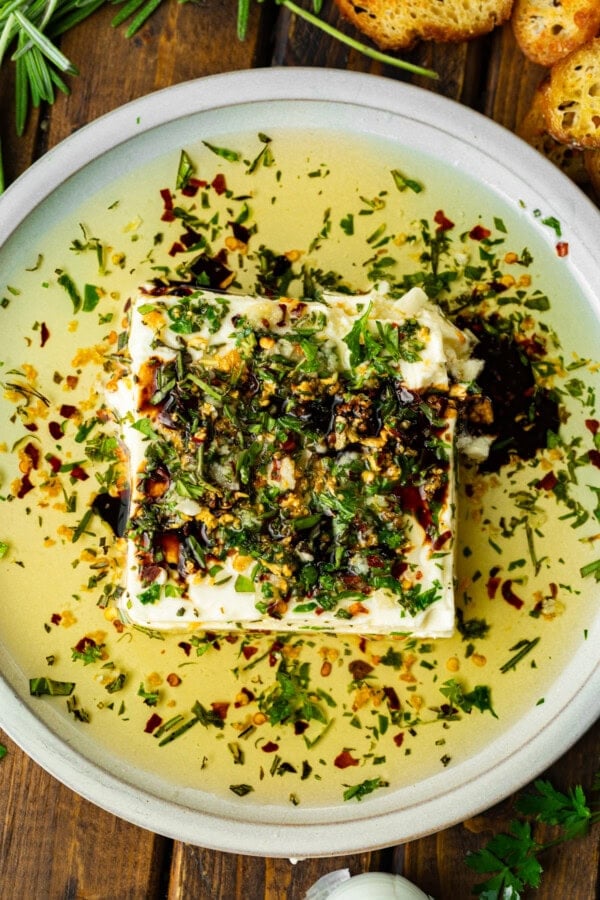 a shallow white circular serving tray with a block of feta cheese topped with sizzling herb oil