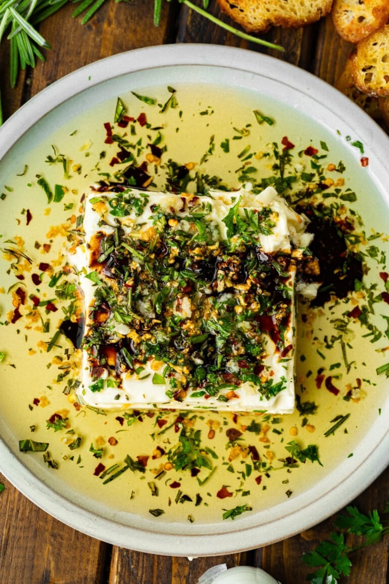 a shallow white circular serving tray with a block of feta cheese topped with sizzling herb oil