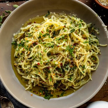 a photo of hot sizzling italian oil over fresh spaghetti and loaded with fresh herbs