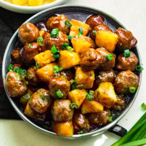 a large serving bowl of saucy hawaiian meatballs mixed with pineapple chunks and topped with chopped green onions
