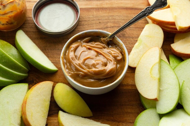 A bowl of sweet dulce de leche sauce is surrounded by sliced apples