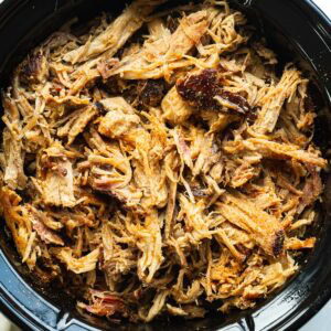 Tender slow cooker pulled pork shredded and piled in a slow cooker.