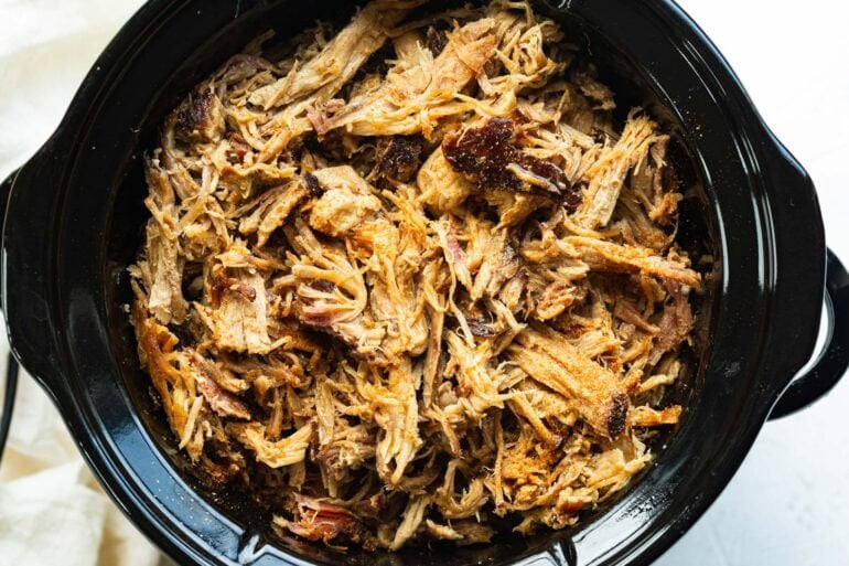 Tender slow cooker pulled pork shredded and piled in a slow cooker.