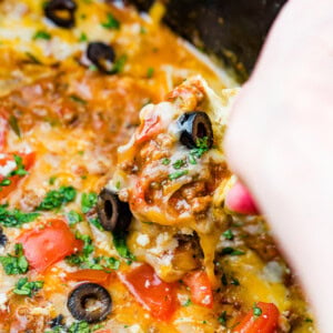 a close up of slow cooker taco dip with a chip scooping some up with olives and fresh cilantro on top