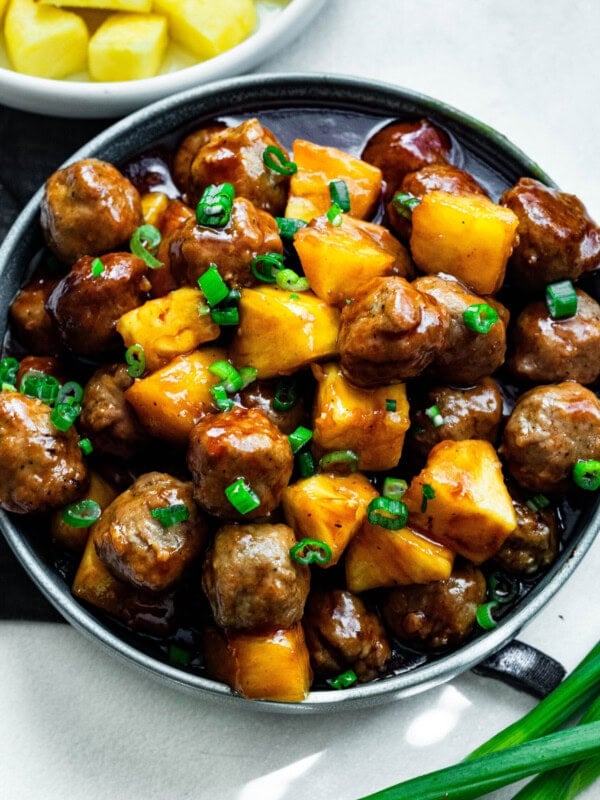a plate of saucy hawaiian meatballs with chunks of pineapple and chopped green onions