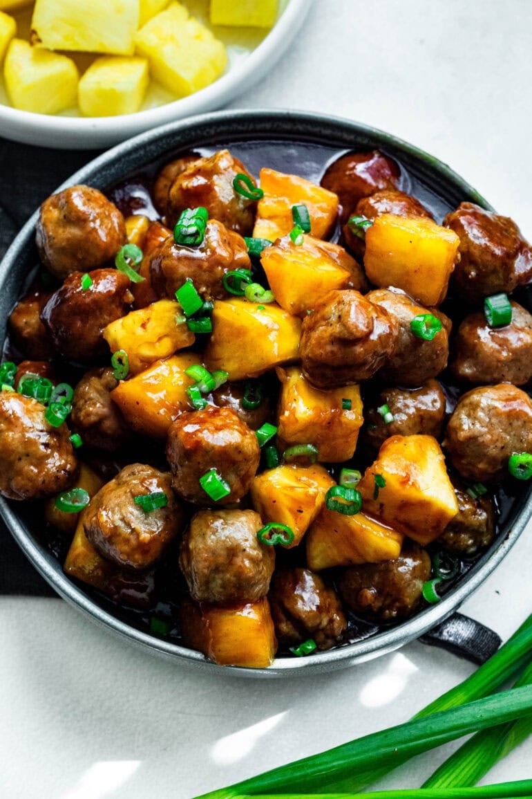 a plate of saucy hawaiian meatballs with chunks of pineapple and chopped green onions