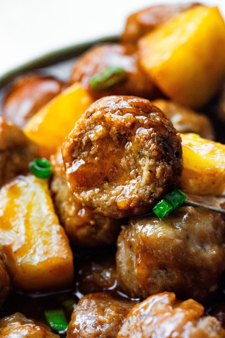 close up of the cross-section of a hawaiian meatball with other meatballs and pineapple chunks around it