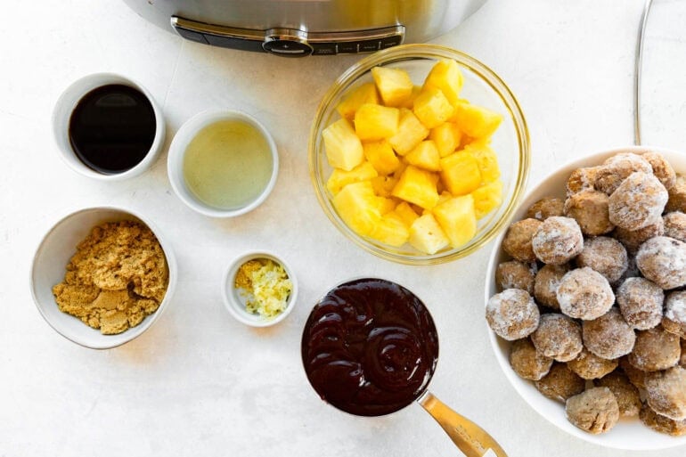 all the ingredients for slow cooker hawaiian meatballs in separate small bowls including bbq sauce, pineapple chunks, frozen meatballs, brown sugar and garlic