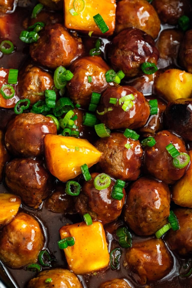 a large pot of saucy hawaiian meatballs with pineapple chunks and chopped green onions