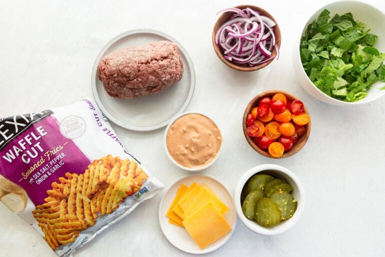 The ingredients for a smash burger bowl including ground beef, red onions, tomatoes, lettuce, cheese, burger sauce