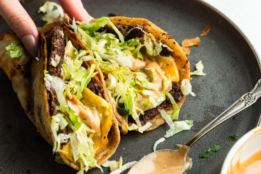 a hand picking up a smash burger taco