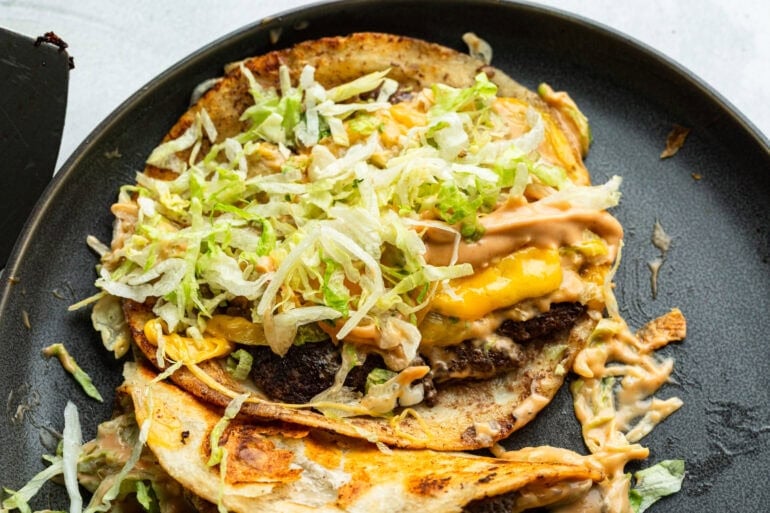 an open smash burger taco topped with melted cheese, shredded lettuce and burger sauce