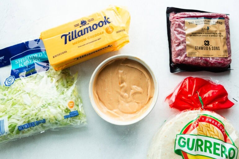 all the ingredients for a smash burger taco including cheddar cheese, flour tortillas, ground beef and shredded lettuce