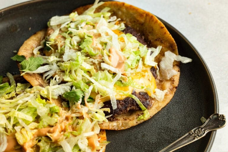 a dinner plate with two smash burger tacos on it