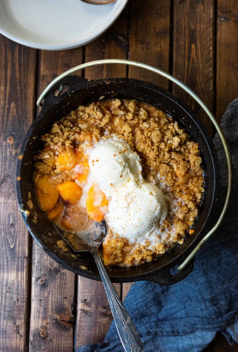 a photo of a cast iron dutch oven with a serving missing and two scoops of vanilla ice cream melting on top.