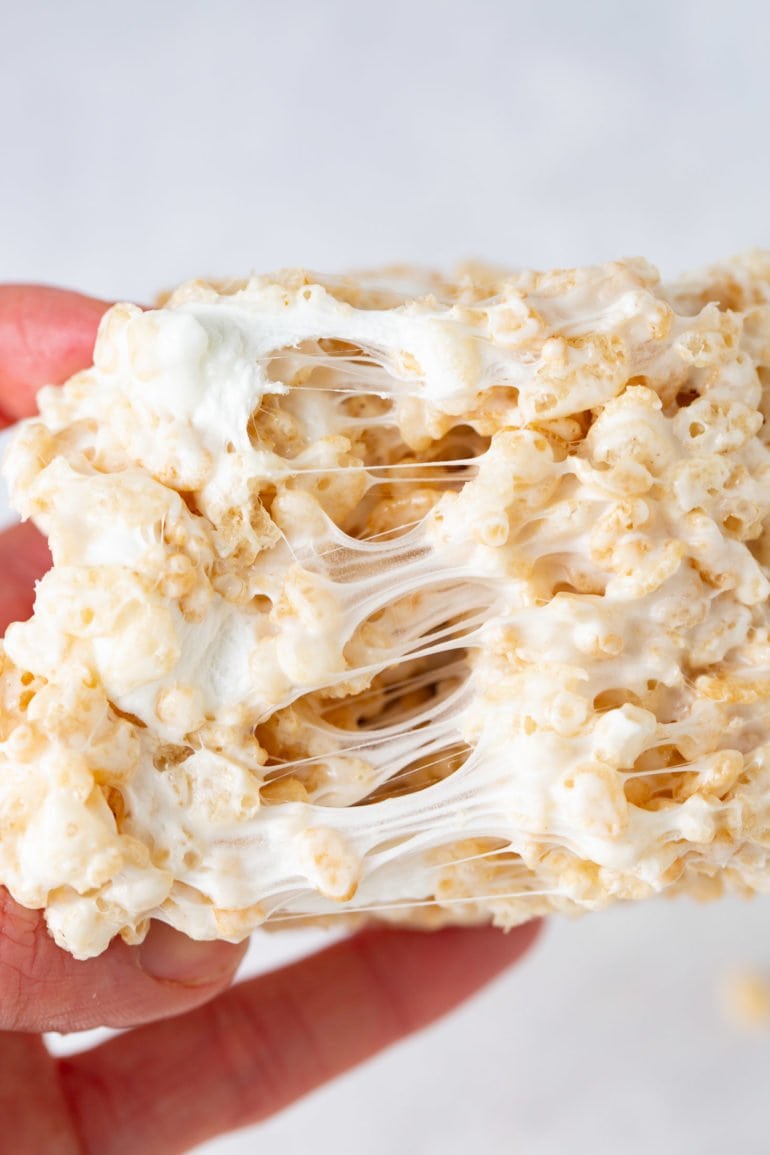 A piece of rice krispie treat that is being pulled apart to show the gooey melted marshmallow holding the rice krispies together.