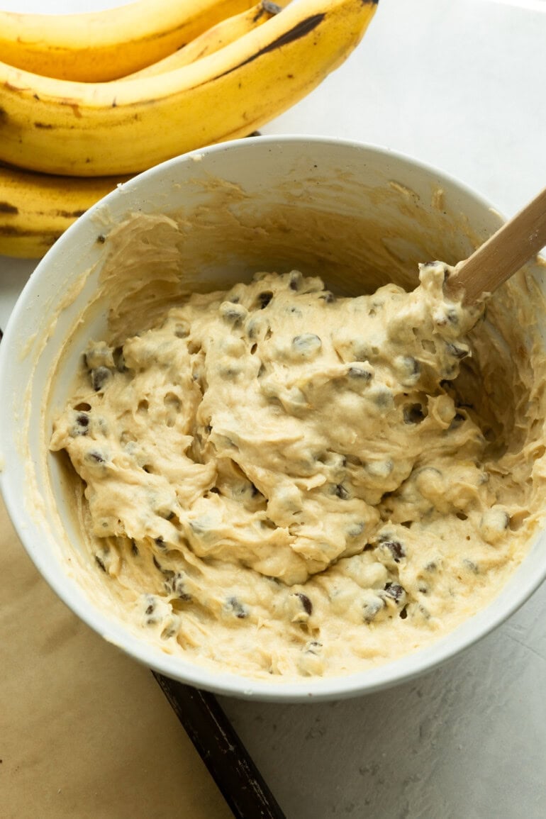 a large mixing bowl full of banana chocolate chip cookie dough being mixed with a wooden spoon