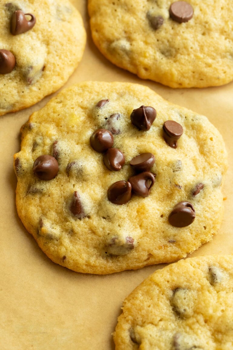 a large golden baked banana cookie with chocolate cips sitting on a brown piece of parchment paper surrounded by more cookies