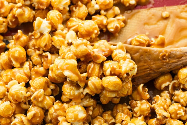Popcorn being tossed with warm caramel sauce on a lined baking sheet