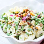 A white bowl with orchiette pasta, peas, cubed colby jack cheese, red onion and a simple dressing for the recipe southern pea pasta salad