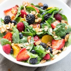 spinach berry salad with brown sugar almonds and lemon dressing 8 scaled A photo of a large ceramic white bowl full of spinach berry salad topped with brown sugar almonds and blackberries, raspberries, and strawberries.