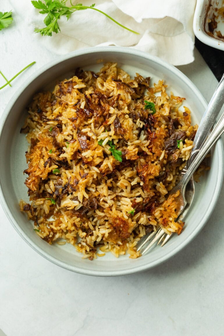 A close-up angle of the baked rice served in a bowl with two forks, showing the glossy, buttery finish and golden-brown edges. You can see the texture clearly, soft, crispy, savory, and packed with flavor.