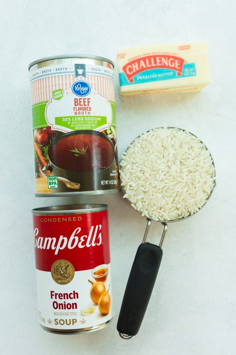 All the ingredients laid out on a counter: long-grain white rice, a stick of butter, a packet of onion soup mix, and a can of beef broth. Simple pantry staples that come together to make a rich, cozy side dish.