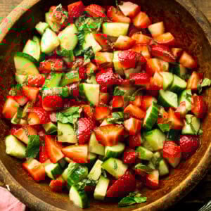 a photo of a wooden serving bowl full of strawberry cucumber salad