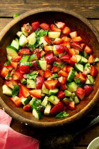 a photo of a wooden serving bowl full of strawberry cucumber salad