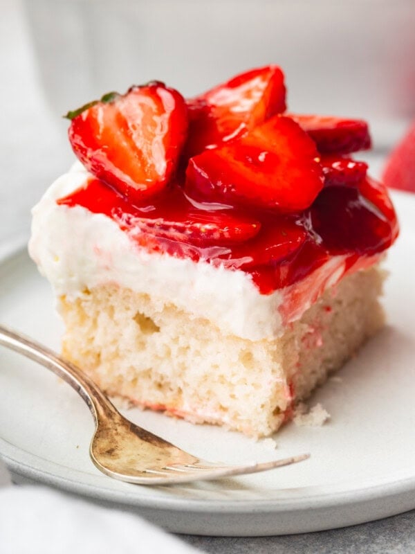 a photo of a single piece of moist white cake on a small dessert plate topped with whipped cream cream cheese frosting and juicy red strawberries