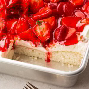 a photo of a single layer white cake topped with cream cheese frosting and juicy red strawberries with some slices removed so you can see the cross section