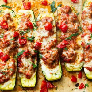 several stuffed zucchini boats topped with melted mozzarella cheese on a piece of brown parchment paper