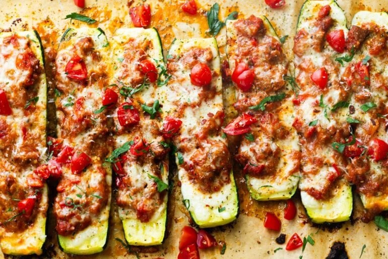 several stuffed zucchini boats topped with melted mozzarella cheese on a piece of brown parchment paper