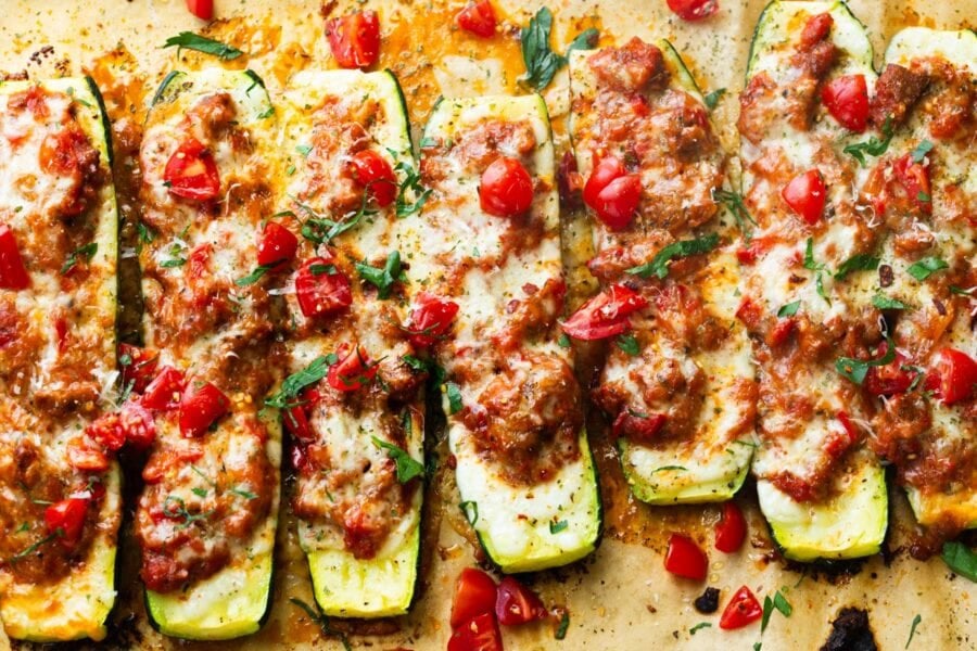 several stuffed zucchini boats topped with melted mozzarella cheese on a piece of brown parchment paper