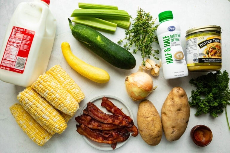 all the ingredients for zucchini corn chowder including corn on the cob, zucchini, potatoes, yellow squash, celery, bacon, onions and fresh herbs