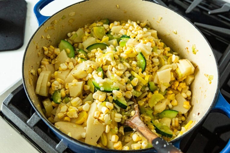 the vegetables in zucchini corn chowder being stirred in a large dutch oven