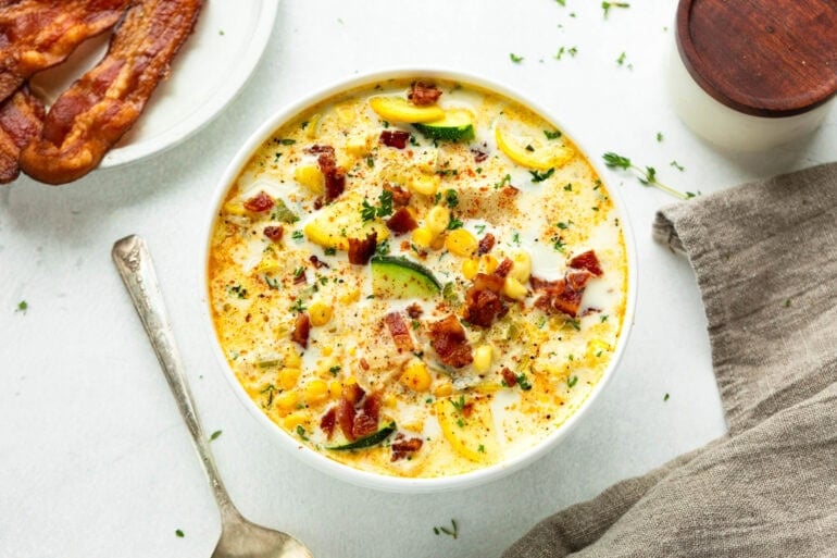 a bowl of creamy zucchini corn chowder topped with crispy bacon bits and sliced green onions