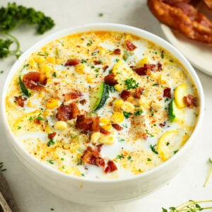 a bowl full of creamy zucchini corn chowder topped with bacon bits and sliced green onions