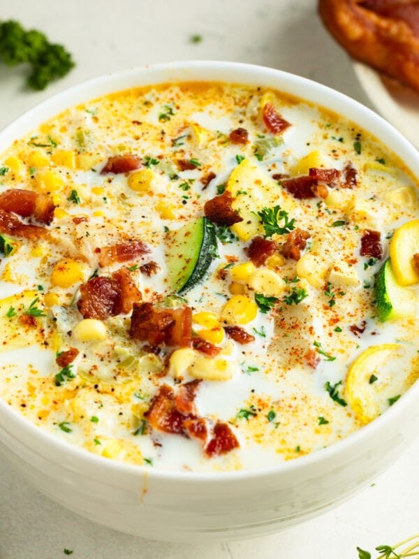 a bowl full of creamy zucchini corn chowder topped with bacon bits and sliced green onions