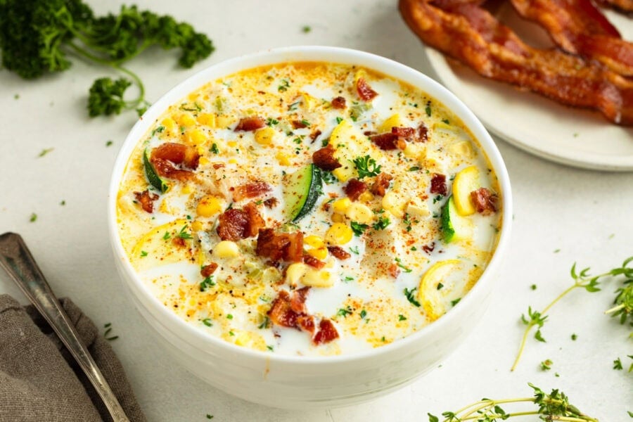 a bowl full of creamy zucchini corn chowder topped with bacon bits and sliced green onions