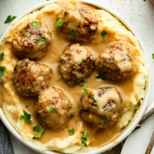 a bowl of creamy Swedish meatballs on a bed of mashed potatoes and sprinkled with fresh parsley