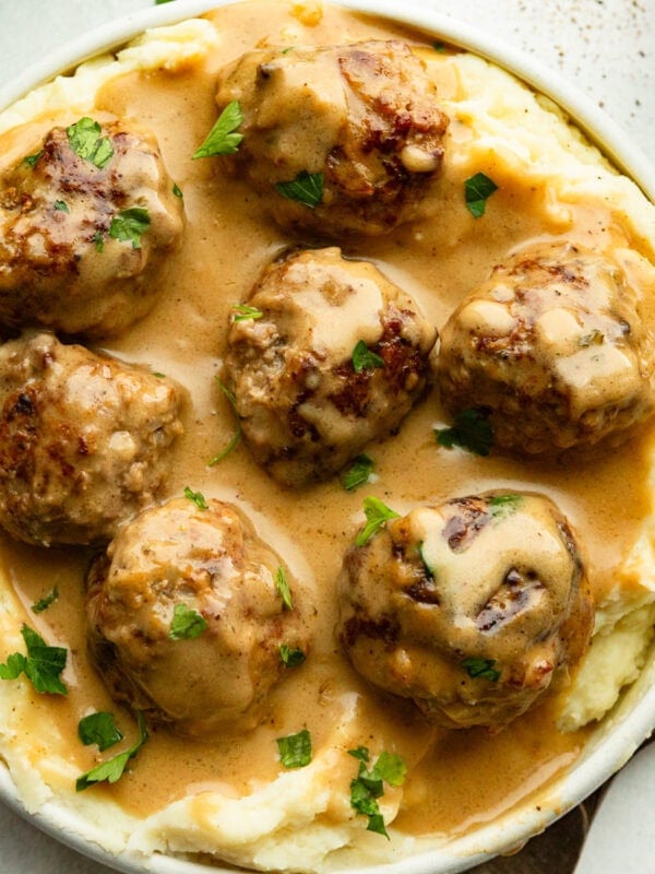 a bowl of creamy Swedish meatballs on a bed of mashed potatoes and sprinkled with fresh parsley