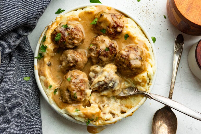 a spoon scooping up a Swedish meatball on top of mashed potatoes