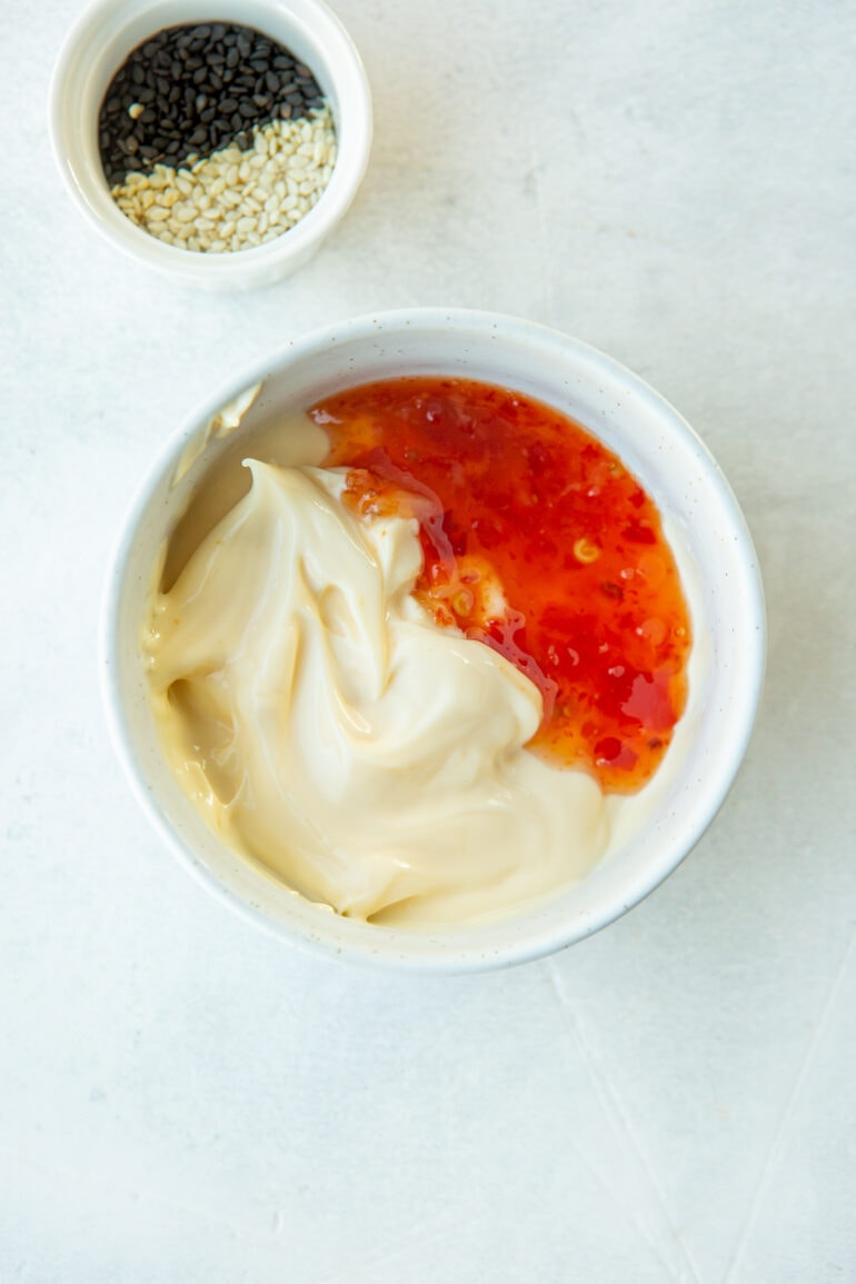 a photo of a small white bowl with mayonnaise and sweet chili sauce it in sitting side by side and not mixed yet.