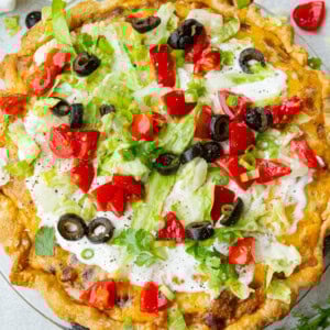 a whole taco pie with a golden crust, cheesy ground beef, topped with sour cream, shredded lettuce, diced tomatoes and black olives